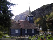 The church is located on the Flåm farm, and it is not a building most visitors associate with Flåm, such as the railway station and the hotel down by the fjord village called Fretheim. The mountain in the background is called Vidmenosi.