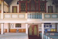 The picture shows parts of the nave, the main entrance, and the gallery with the organ.