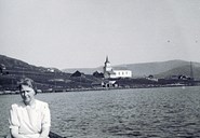 Agnes Jørgensen in a row boat on the bay of Kalvågvika. In the background we see the landscape of Frøyalandet and Frøya church at Kalvåg. The church, completed in 1865, was the only one in the Bremanger municipality until 1904. 