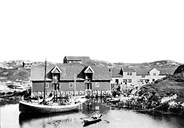 From the good and sheltered harbour at Gåsvær. The fishing vessel is the <b>Firda.</b> Hans P. Gåsvær is sitting in the Nordfjord rowboat. To the right, the big residential building can be seen, and to its left the sea warehouse from 1904.