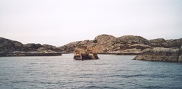 A part of the stem of this cement boat juts out of the sea in a bay on the south side of Ospa. Two boats were built of concrete, it is believed in 1929. It was also said that they were built in the Osterfjord. One of them was so heavy that they could not get it off the slip. The other one was put in operation, with a new engine.<br />
Perhaps it was on the first trip north that they came off course across the Lågøyfjord, so that the boat touched the sea floor, to the west of Hamnholmen, it is believed. She sprang a leak, and they looked for a cove to strand it in. Unfortunately there was an underwater rock where they tried, so the boat stopped short of where they had hoped to land. She took in water, and the stern sank.<br />
The company Olav Aalen from Kvammen took on diving assignments and salvaged the engine, a 150 HP 2 cylinder Bolinder, which Fylkesbaatane (steamship company) bought at a reasonable price. They installed the engine in the M/B "Nesøy." The engine worked flawlessly for 27 years.