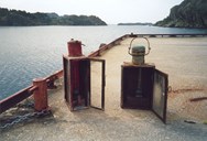 Except in broad daylight, the lights at the steamship terminal had to be lit and in place in due time before the steamship approached. The picture shows the lights used for many years at the Steinsund quay. The two ten-line paraffin lights were lit in the tiny post office in the shed of the terminal. The glass of the lights had to be cleaned of carbon deposit every day when the steamer called, if there had been a strong wind. The light with a red door was placed farthest south on the corner of the quay. Thus the captain could see the direction of the quay and had no difficulty docking.