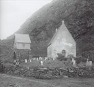 The location and the architecture of the Kinna church is unique, and it is the only church built in stone in the region of Sunnfjord. There is no clear explanation why such a costly building was located here on a mountainous island far out by the open sea. The answer, however, must be found in what was the origin of the legend material linked to Borni and St. Sunniva. To the left the belfry which was built on a stone vault in the last restoration in 1911-1912.
