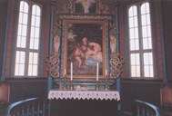 The altarpiece from 1912 depicts Joseph and Mary with the Holy Infant, and John the Baptist with his characteristic staff cross.  There is a glimpse of the river Jordan to the left, and the mountains in the background are probably Lebanon and Hermon. The framework is carved and richly decorated by Kinsarvik. On the altar there are four brass candlesticks.